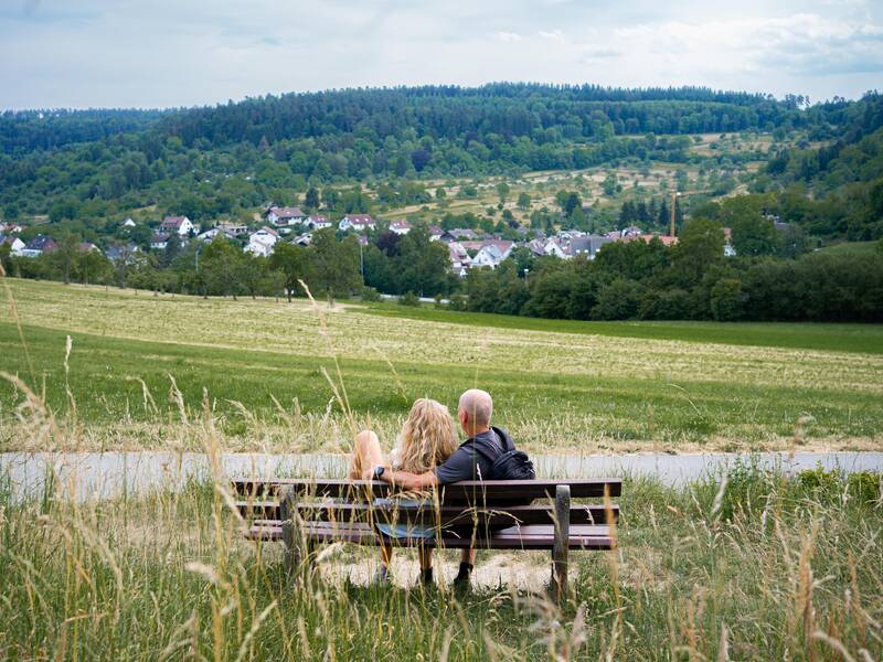 Eine Frau und ein Mann sitzen auf einer Bank in der Natur.